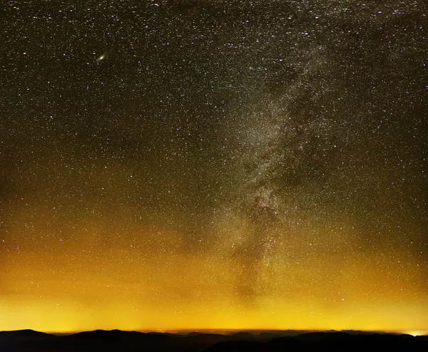 Samanyolu üzerinde kara dağlar ve şehir ışıkları