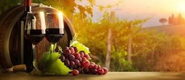 İki kadeh kırmızı şarap ahşap masada, üzümlü ve fıçılı, İtalya sonbaharı manzaralı.