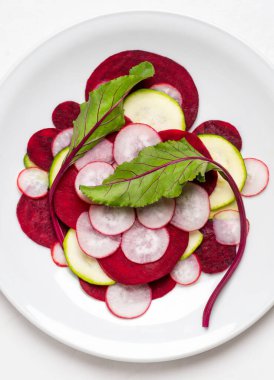 Pancar yaprakları beyaz bir tabakta ince pancar, turp ve kabak dilimlerinde ve beyaz arka planda.