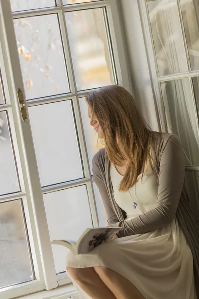 Mujer joven leyendo por la ventana — Foto de Stock