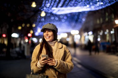 Noel zamanı sokakta cep telefonunu kullanan güzel genç bir kadın.
