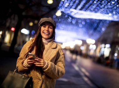 Noel zamanı sokakta cep telefonunu kullanan güzel genç bir kadın.