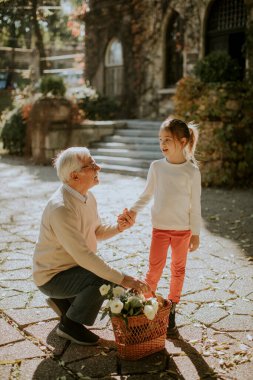 Büyükbabası küçük tatlı torunuyla eğleniyor ve elinde çiçek dolu bir sepet tutuyor.