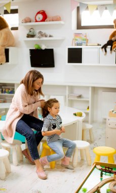 Kreş öğretmeni, küçük tatlı kızın anaokulunda saç düzeltmesine yardım ediyor.