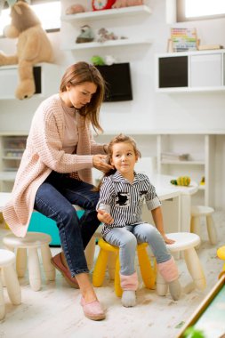 Kreş öğretmeni, küçük tatlı kızın anaokulunda saç düzeltmesine yardım ediyor.