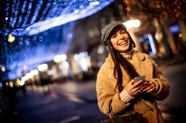 Noel zamanı sokakta cep telefonunu kullanan güzel genç bir kadın.