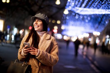 Noel zamanı sokakta cep telefonunu kullanan güzel genç bir kadın.