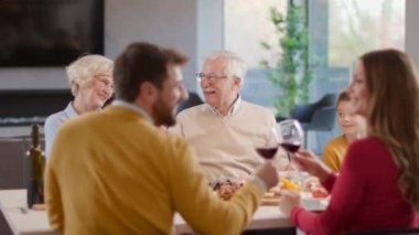 Mutlu bir aile evde kırmızı şarapla yemek yiyor.