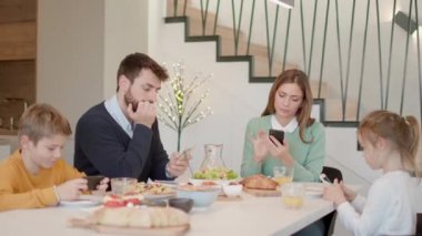 Aile, evdeki yemek masasında kahvaltı ederken cep telefonu kullanıyor.