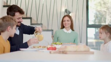 Genç mutlu aile, evdeki yemek masasında kahvaltı ederken konuşuyor.