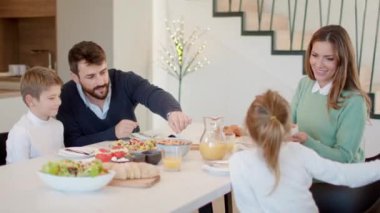 Genç mutlu aile, evdeki yemek masasında kahvaltı ederken konuşuyor.