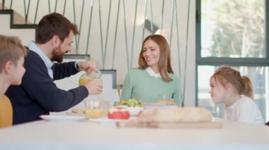 Genç mutlu aile, evdeki yemek masasında kahvaltı ederken konuşuyor.