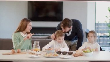 Genç mutlu aile, evdeki yemek masasında kahvaltı ederken konuşuyor.