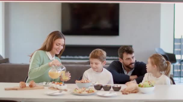 アパートのダイニングテーブルで朝食を食べながら話している若い幸せな家族 — ストック動画