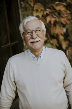 Sağlıklı kıdemli adam, sonbahar günü pencerenin yanında duruyor.