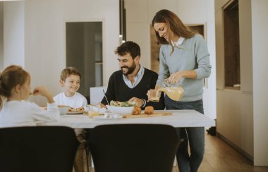Genç mutlu aile, evdeki yemek masasında kahvaltı ederken konuşuyor.