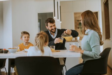 Genç mutlu aile, evdeki yemek masasında kahvaltı ederken konuşuyor.