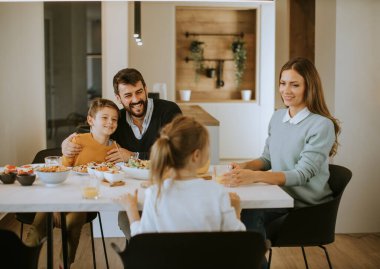 Evdeki yemek masasında yemek yerken genç mutlu aile sohbeti.