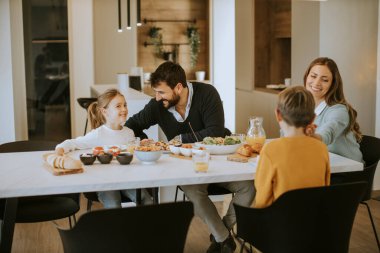Evdeki yemek masasında yemek yerken genç mutlu aile sohbeti.