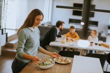 Genç anne modern mutfakta ailesine kahvaltı hazırlıyor.