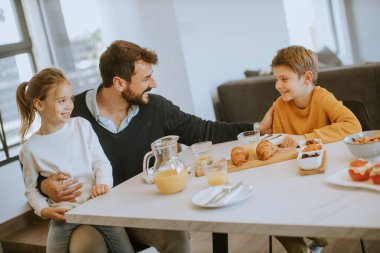 Genç baba, oğlu ve kızıyla kahvaltı yapıyor.