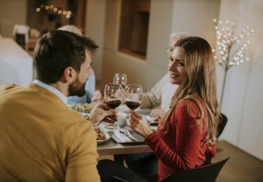 Mutlu bir aile evde kırmızı şarapla yemek yiyor.