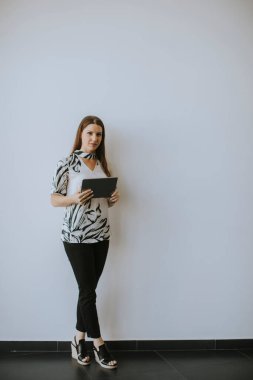 Ofisin duvarında dijital tablet kullanan genç bir iş kadını.