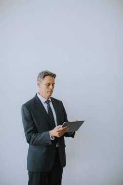 Olgun iş adamı ofisteki duvarın yanında dijital tablet kullanıyor.