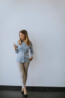 Ofisin duvarında cep telefonu kullanan genç bir iş kadını.