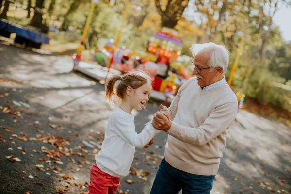 Büyükbaba eğlence parkında küçük tatlı torunuyla eğleniyor.
