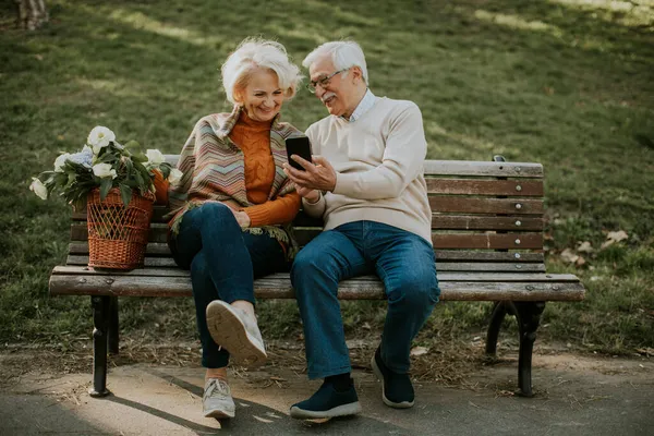 Красивая Пожилая Пара Сидит Скамейке Корзиной Цветов Смотрит Мобильный Телефон — стоковое фото