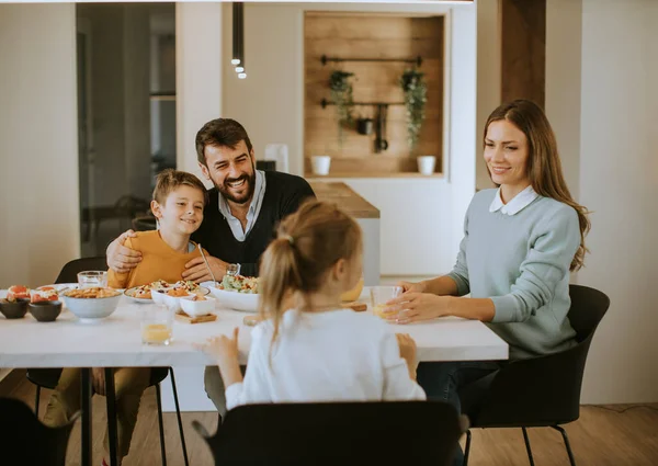 Evdeki yemek masasında yemek yerken genç mutlu aile sohbeti.