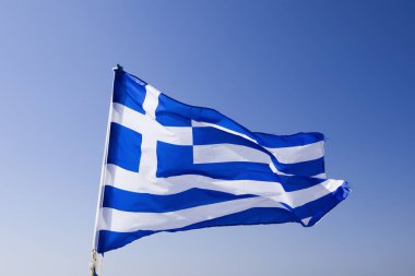 Mavi Akdeniz gökyüzünün altında dalgalanan Yunan bayrağı