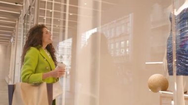 Alışveriş torbası ve kahve fincanı olan güzel kıvırcık saçlı kadın.