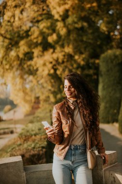 Güneşli bir sonbahar gününde parkta cep telefonu olan güzel bir kadın.