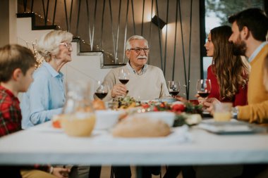 Mutlu bir aile evde kırmızı şarapla yemek yiyor.