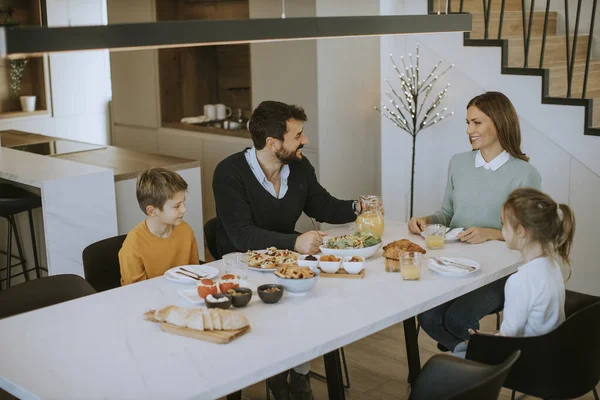 アパートのダイニングテーブルで朝食を食べながら話している若い幸せな家族 — ストック写真