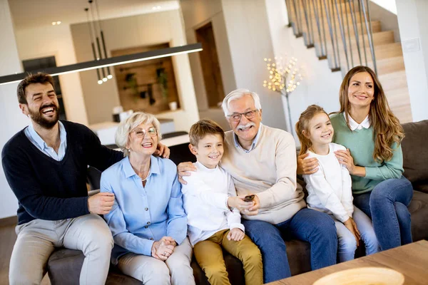 Multi generation family sitting together on the sofa at modern home and watching TV