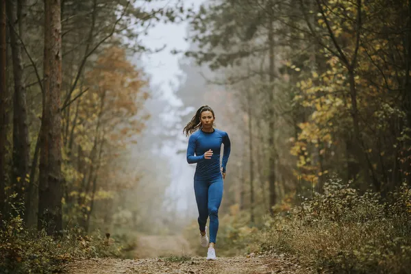 Młoda Kobieta Niebieskim Dresie Biegnie Jesienią Kierunku Kamery Leśnym Szlaku — Zdjęcie stockowe