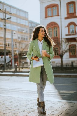 Sokakta akıllı telefon kullanan ve elinde kahve tutan güzel bir kadın.