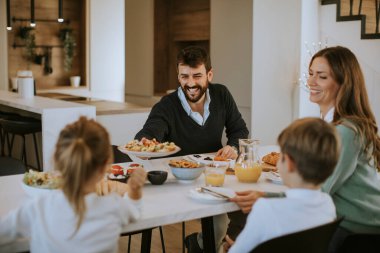 Genç mutlu aile, evdeki yemek masasında kahvaltı ederken konuşuyor.