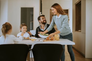Genç mutlu aile, evdeki yemek masasında kahvaltı ederken konuşuyor.