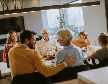 Mutlu bir aile evde kırmızı şarapla yemek yiyor.
