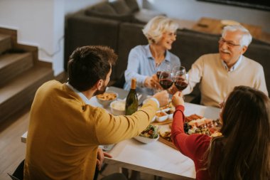 Mutlu bir aile evde kırmızı şarapla yemek yiyor.