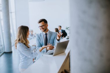 Genç iş çifti ofiste, takımlarının önünde dizüstü bilgisayarla çalışıyor ve tartışıyorlar.