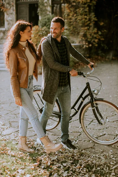 一对年轻貌美的夫妇骑着自行车在秋天的公园里散步 — 图库照片