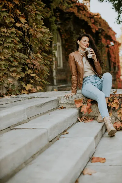秋の日に屋外の階段でテイクアウトコーヒーを飲むかなり若い女性 — ストック写真