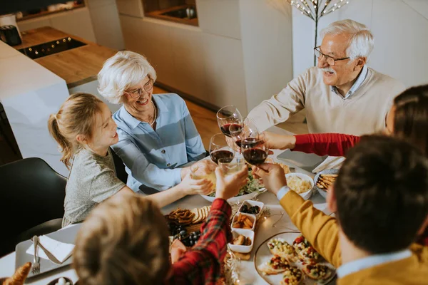 Mutlu bir aile evde kırmızı şarapla yemek yiyor.