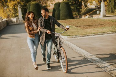Güz parkında bisikletle yürüyen yakışıklı genç çift.