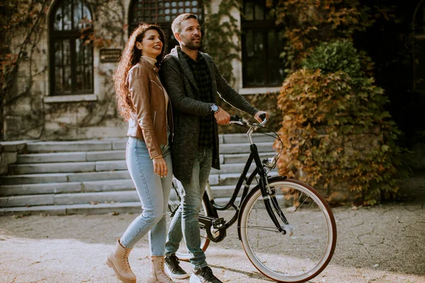 一对年轻貌美的夫妇骑着自行车在秋天的公园里散步 — 图库照片